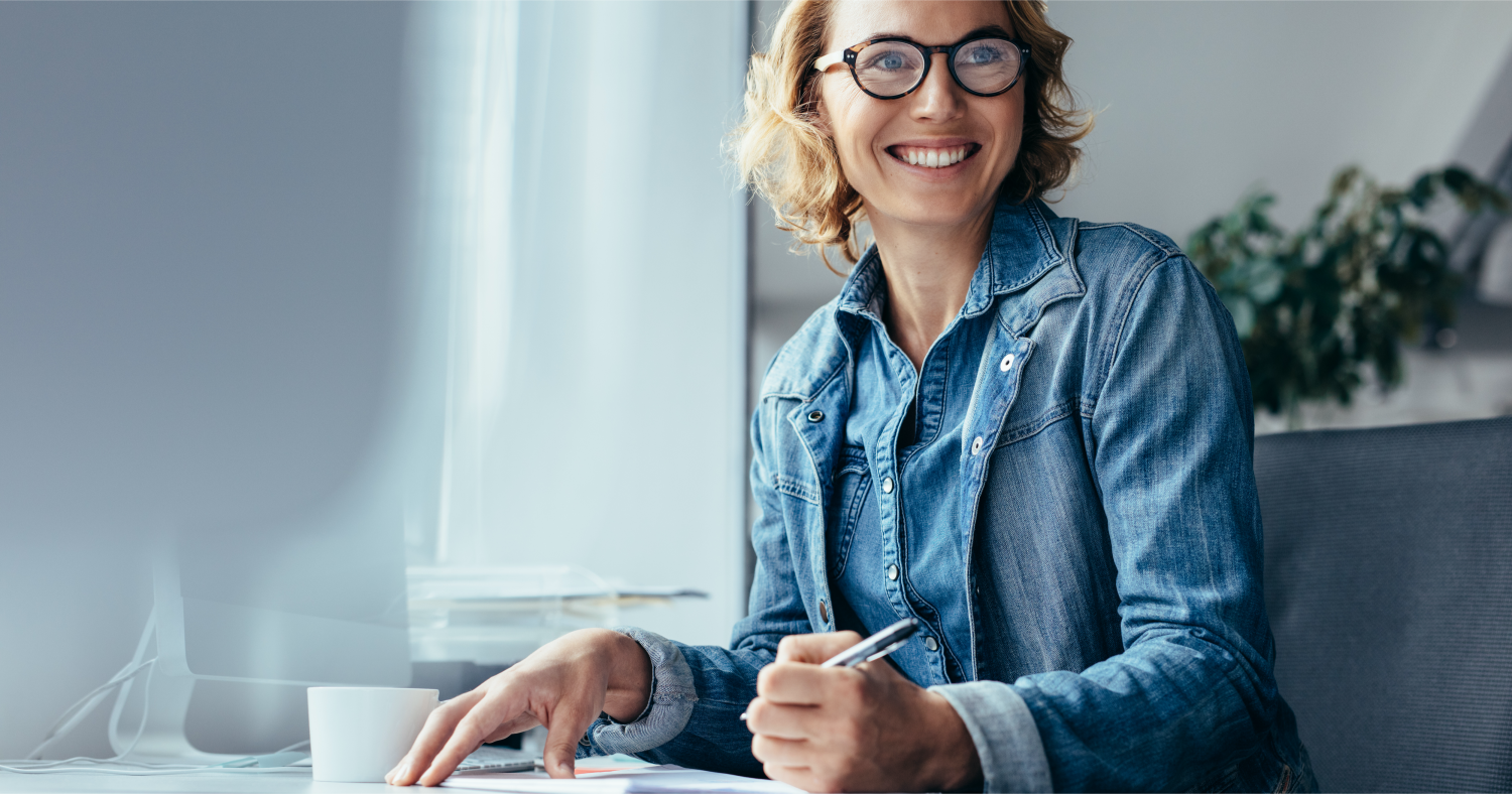 A woman in a blue denim shirt working at a desk in a naturally lit office
