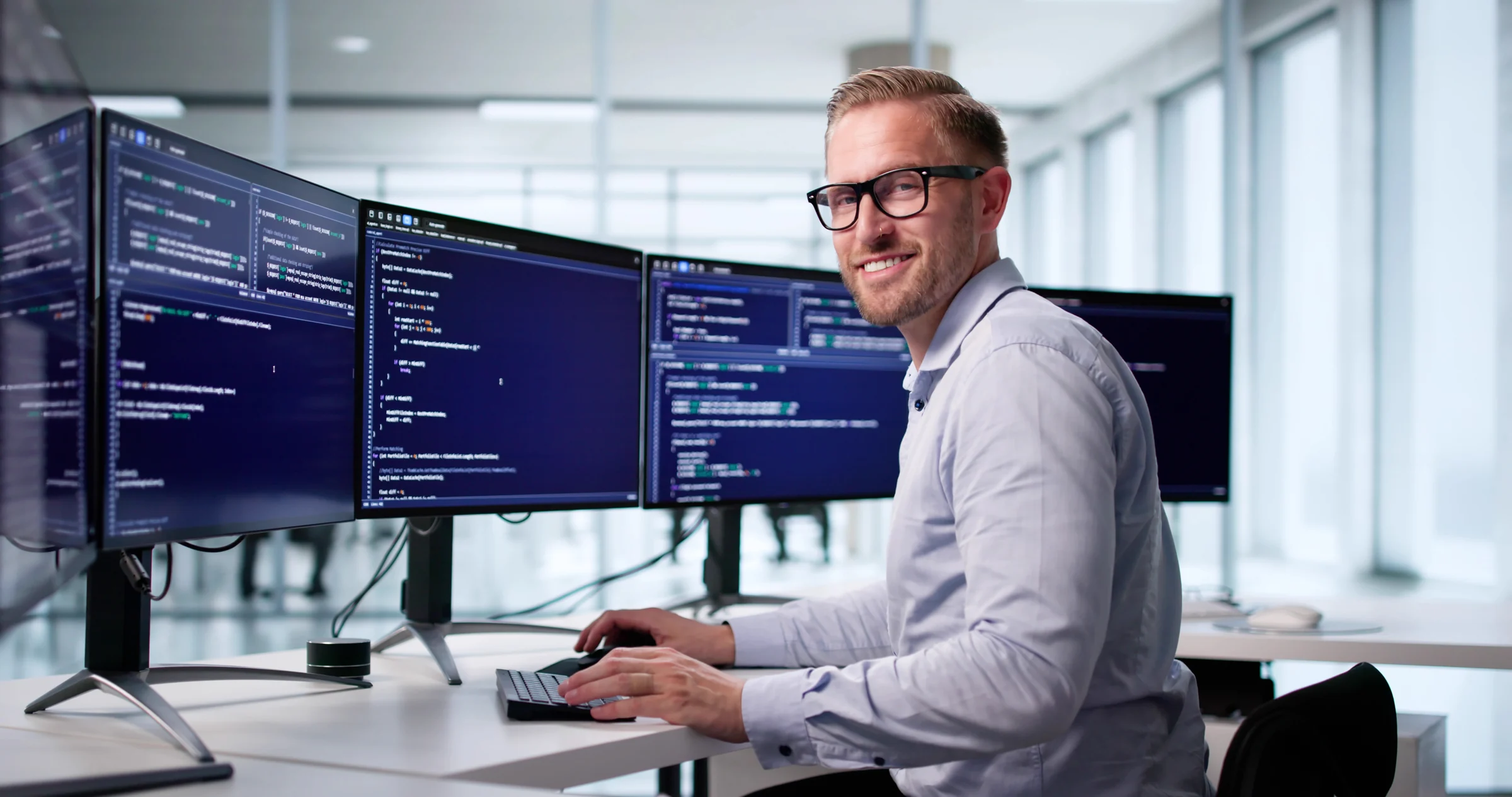 A software developer working at three monitors displaying code.