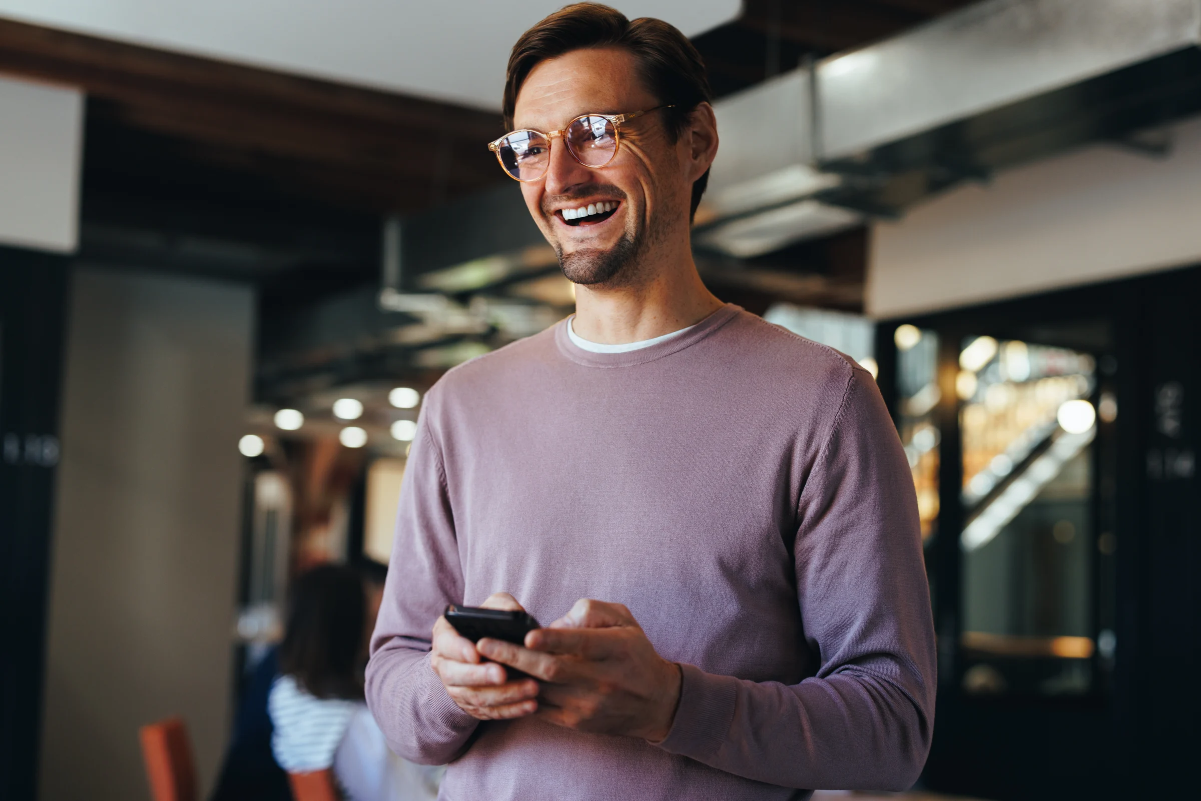 A smiling professional holding his smartphone in a shared workspace