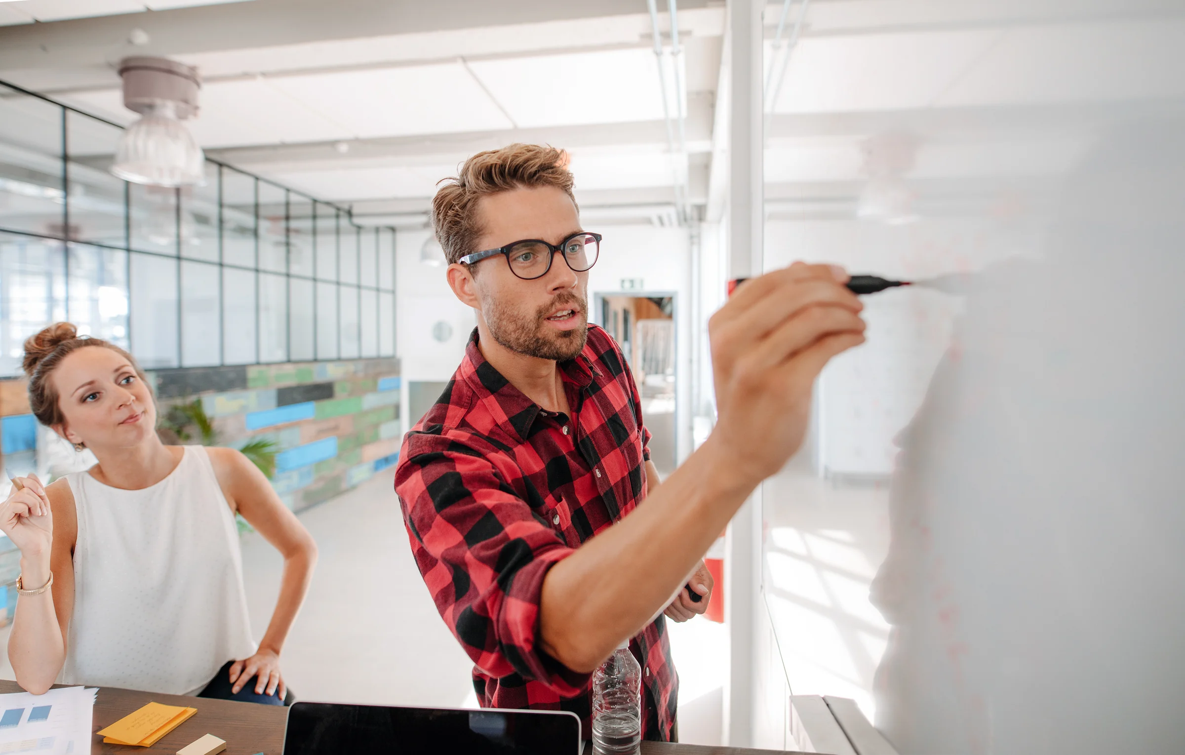 A developer in a red checked shirt planning on a whiteboard with a colleague.