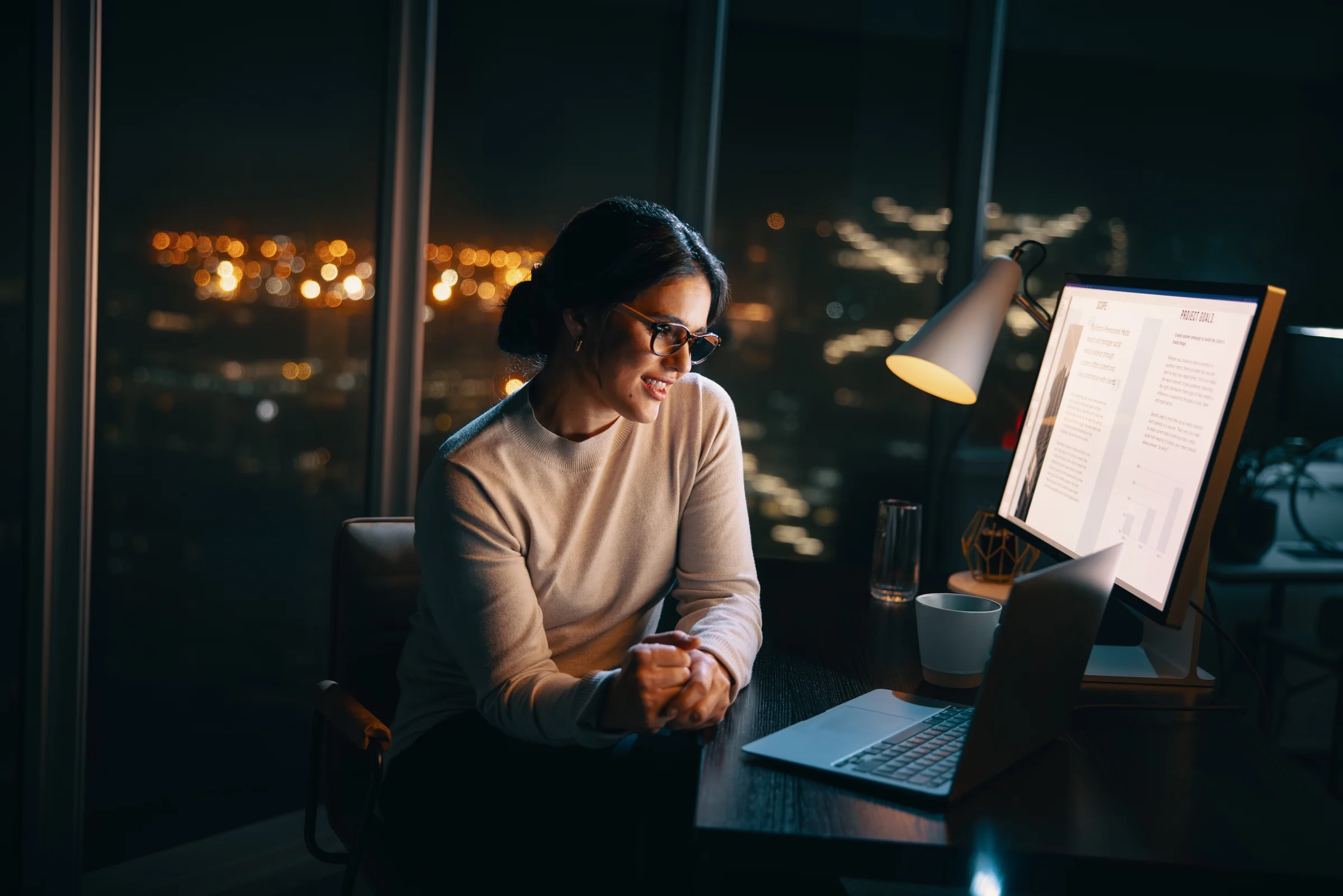 A professional working at a desktop computer in a softly lit office after dark