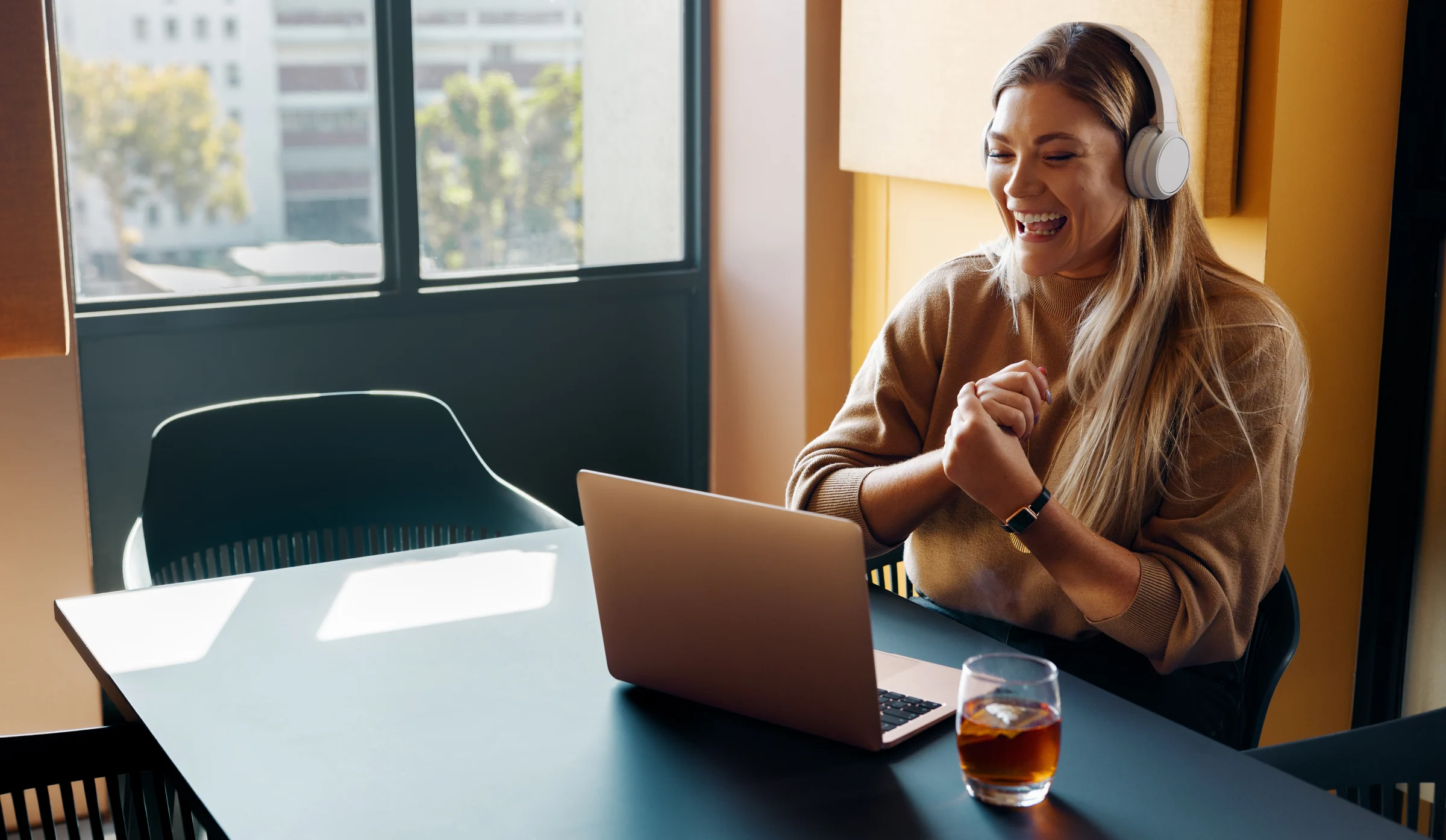 A woman wearing headphones smiling during a laptop call in a warm workspace