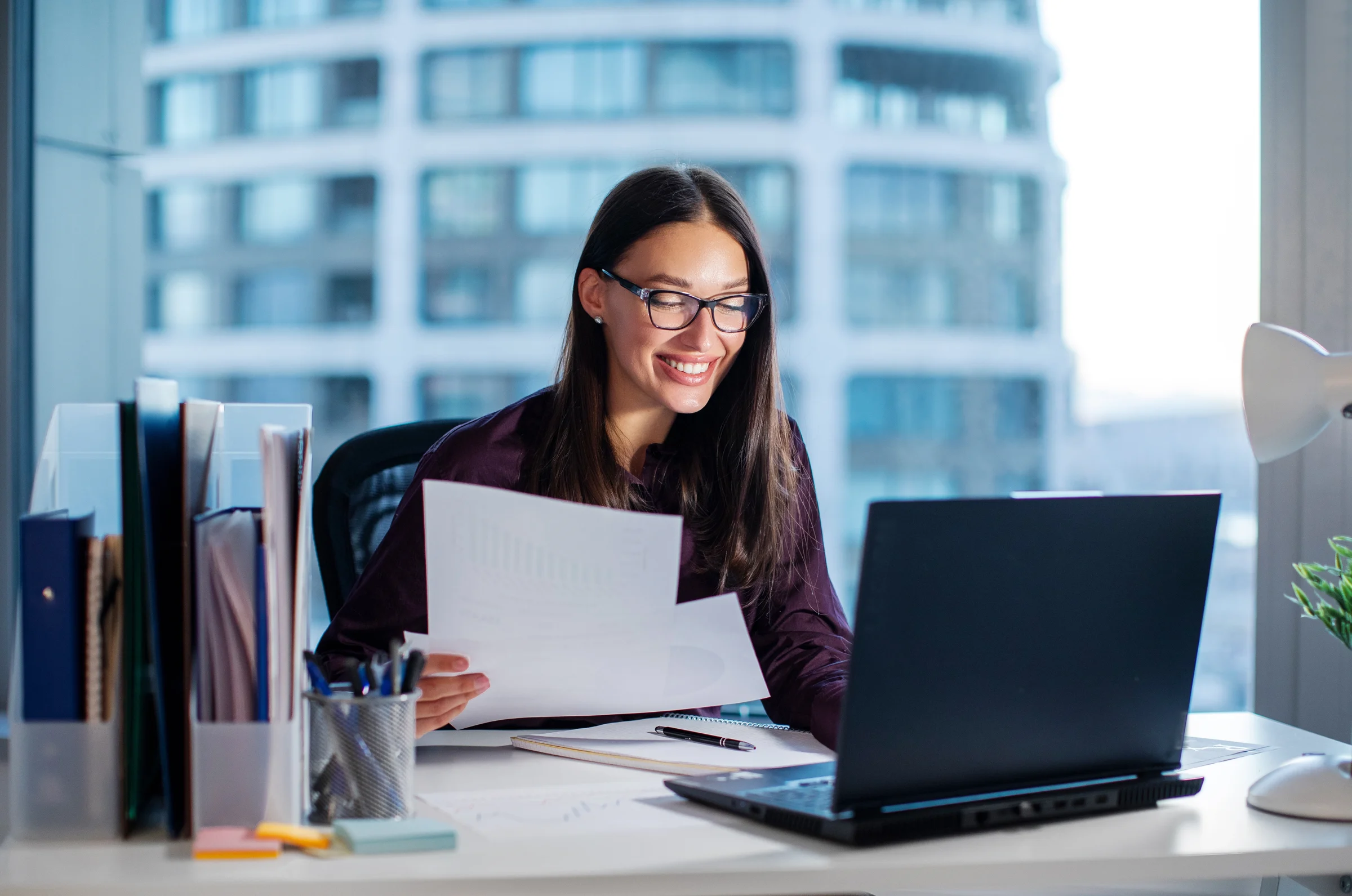A professional reviewing printed documents beside her laptop in an office