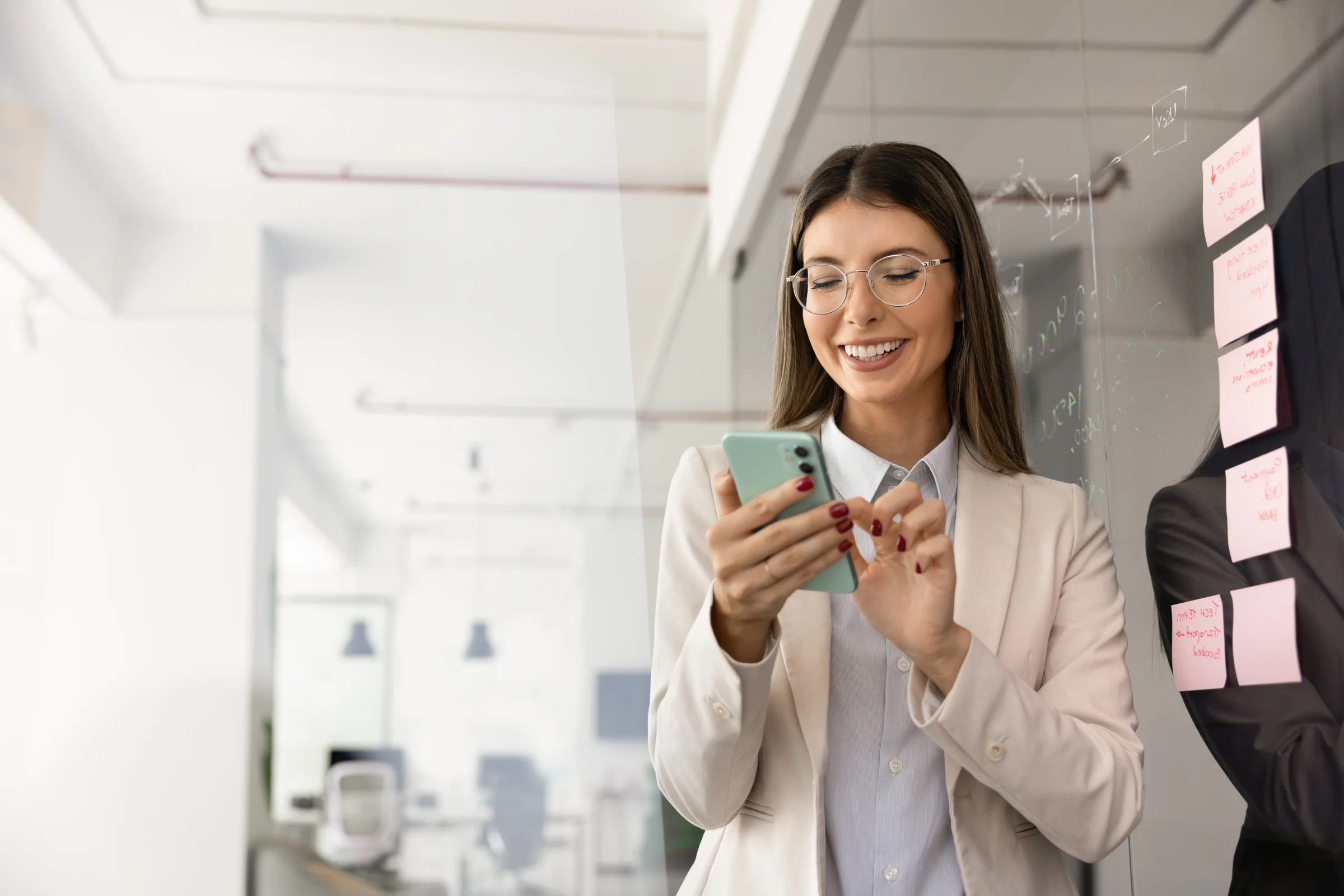 A professional checking her phone beside a planning board covered with notes.