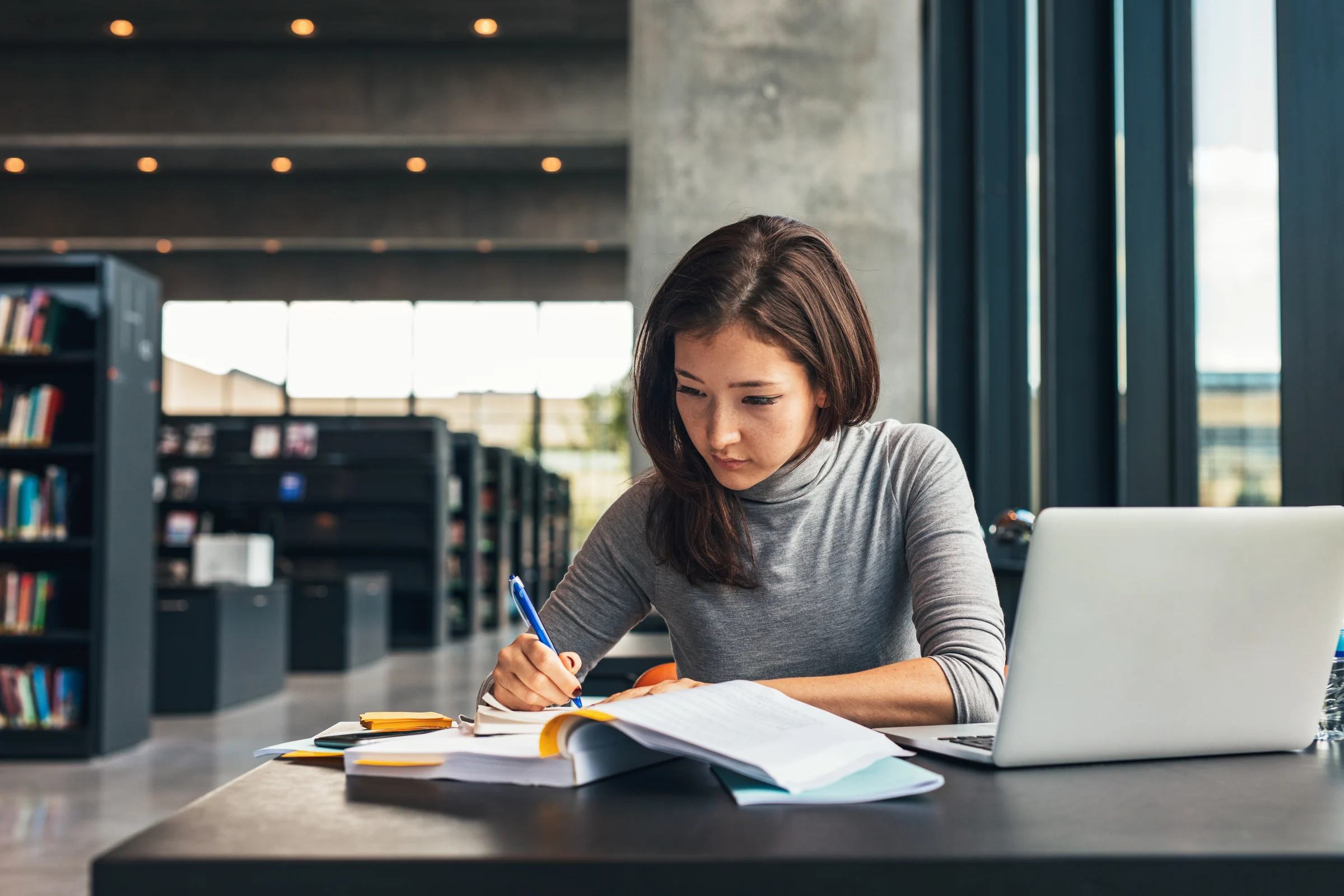 A professional reviewing printed notes beside a laptop in a shared workspace.