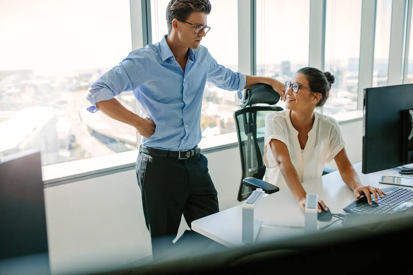 Colleagues discussing a task beside an office workstation