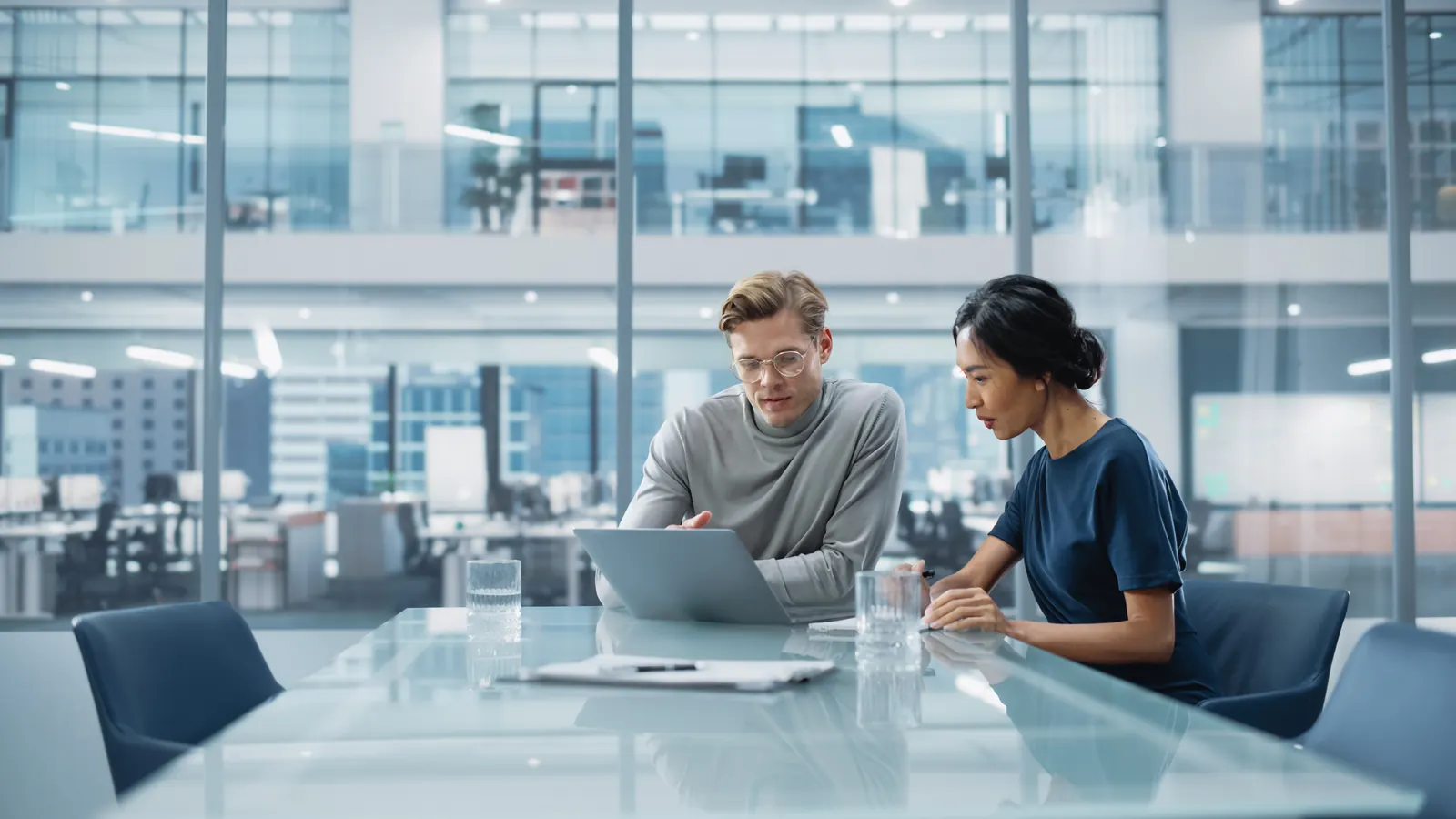 Two colleagues reviewing information on a laptop in a blue-toned meeting room