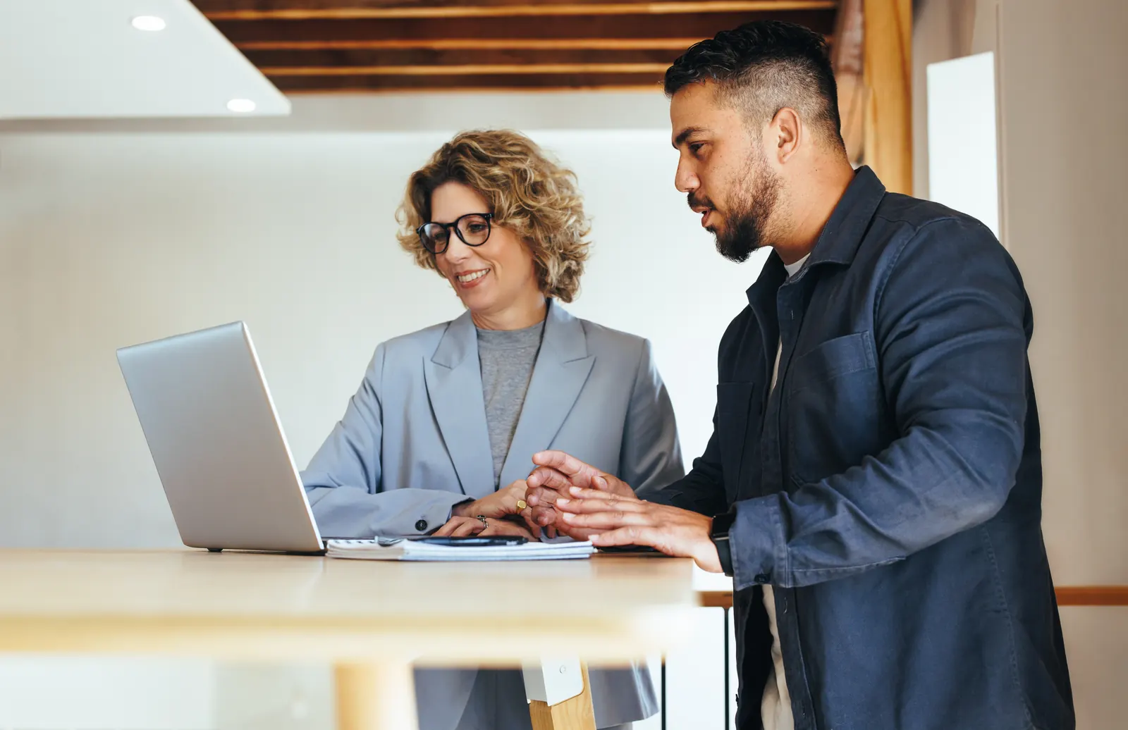 Two business professionals reviewing a laptop together at a high table