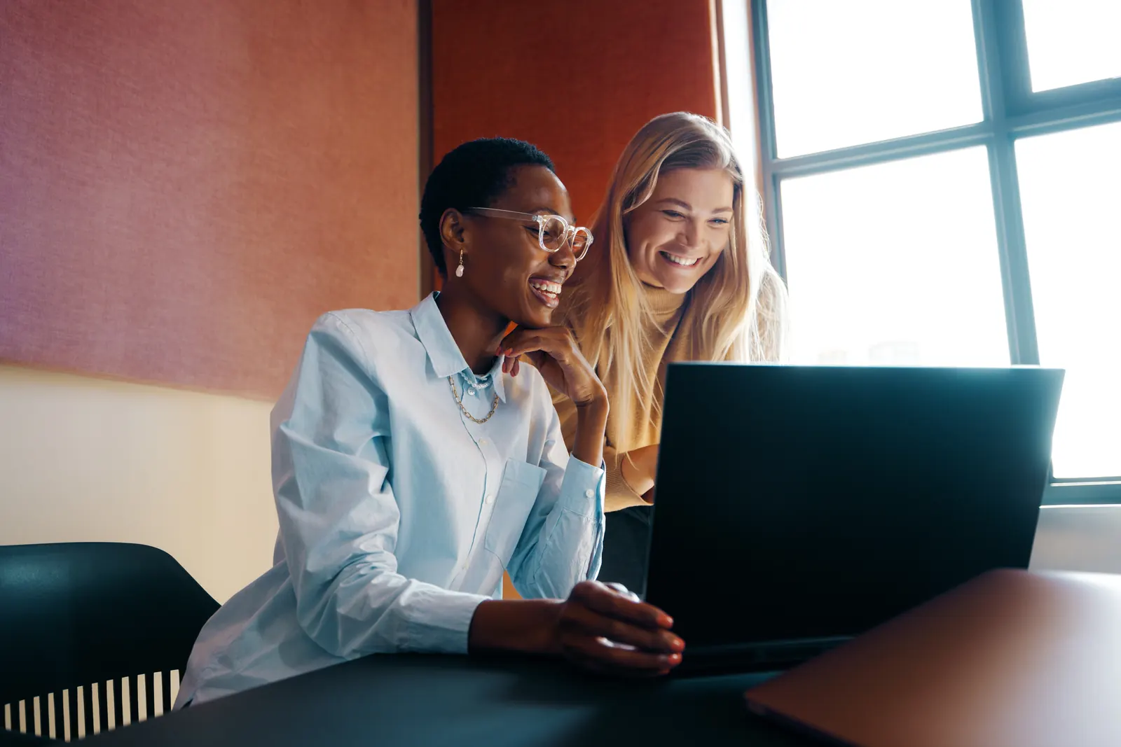 Two specialists reviewing a laptop together beside an office window