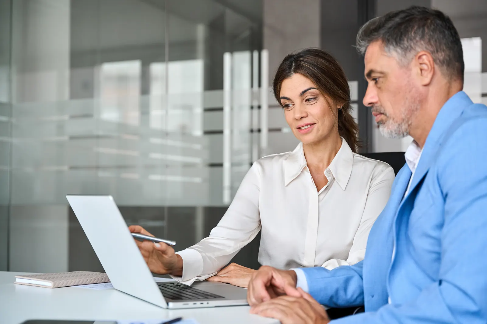 Two colleagues reviewing information together on a laptop in a glass-walled office