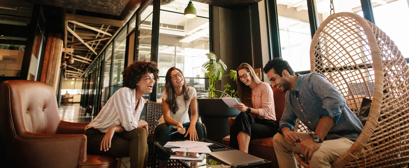 Colleagues discussing notes around a low table in a naturally lit workspace with warm wood and leather seating