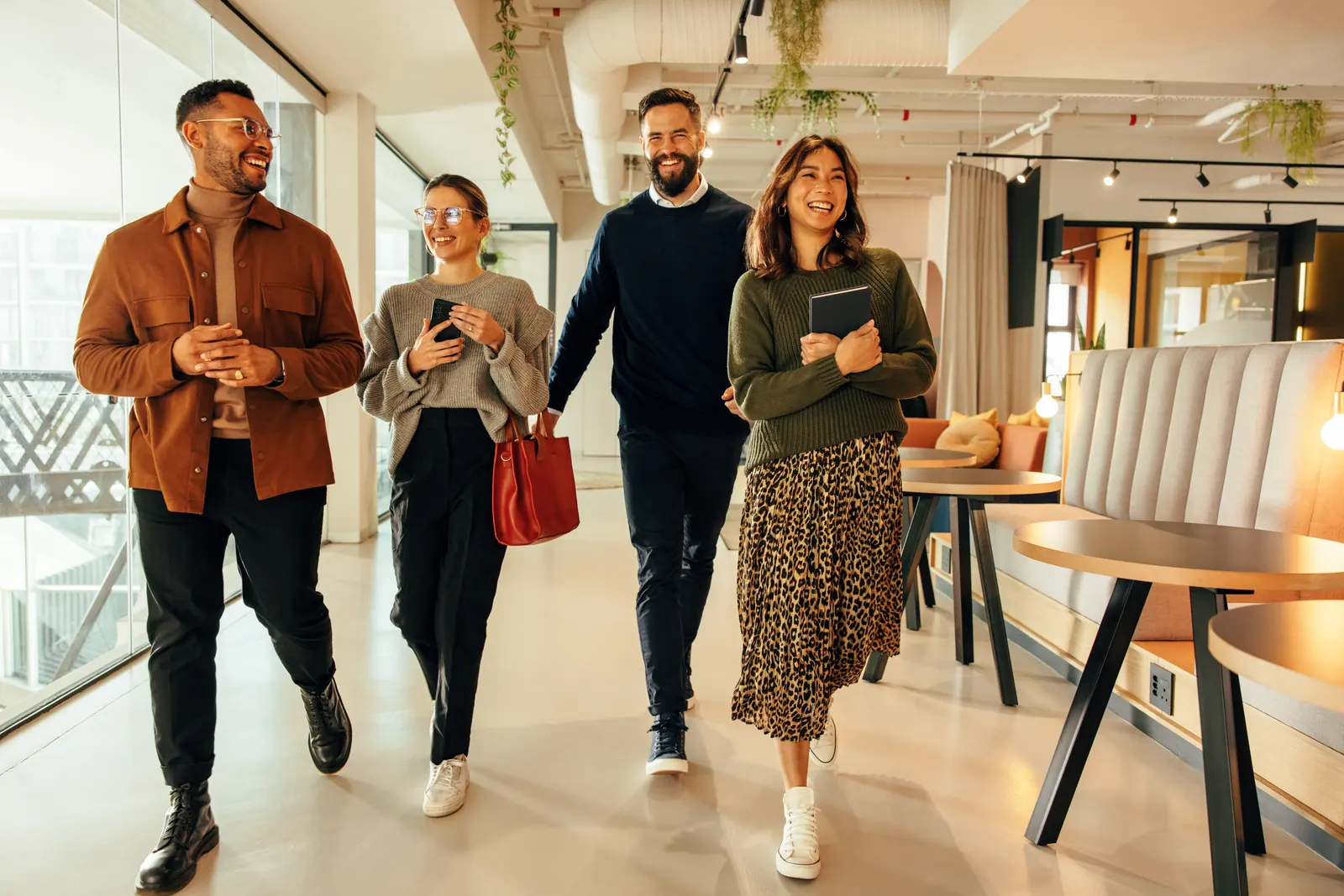 Four colleagues walking through a shared office, one wearing an orange shirt