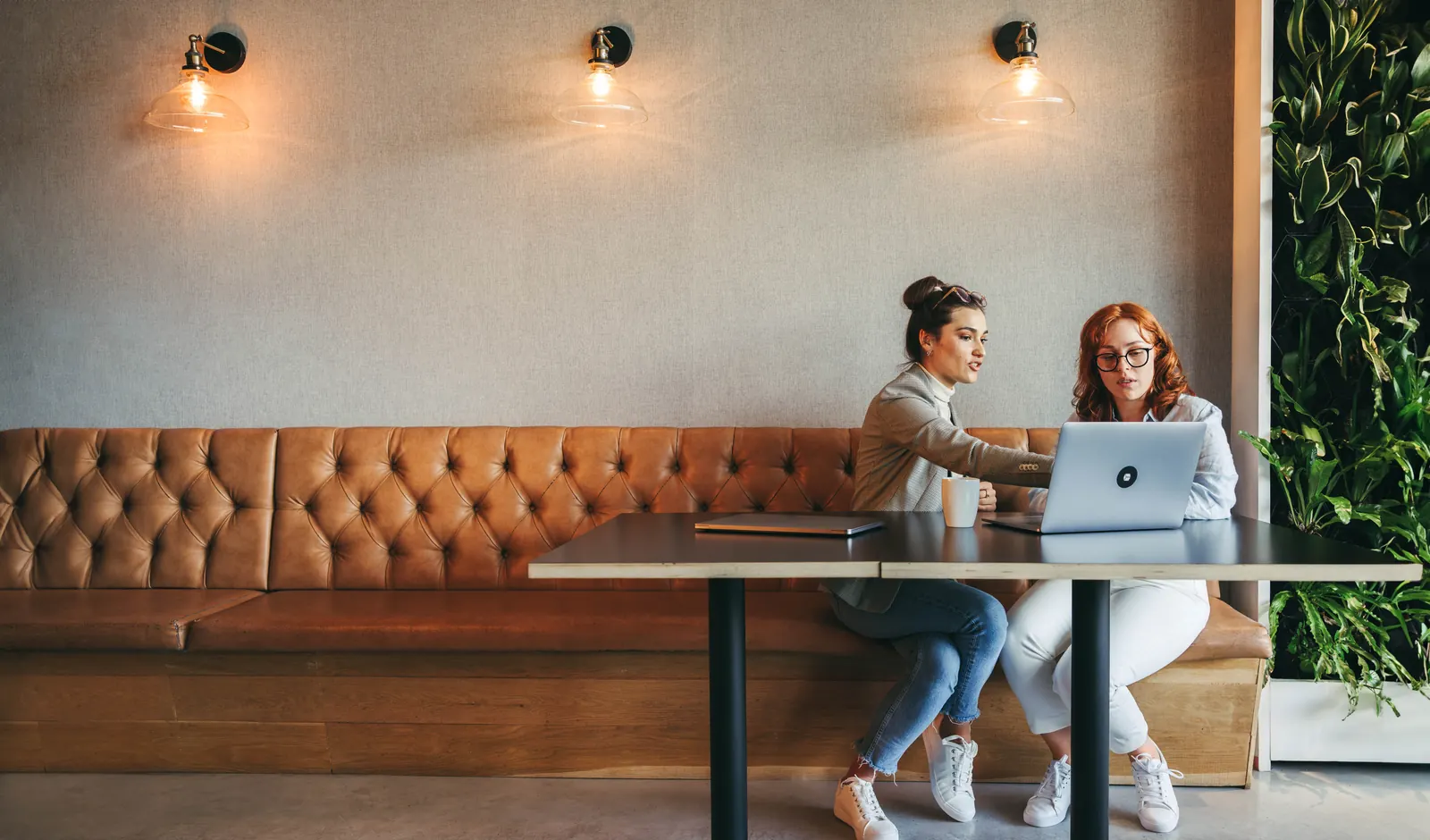 Two colleagues discussing information on a laptop in a warm workspace with tan seating