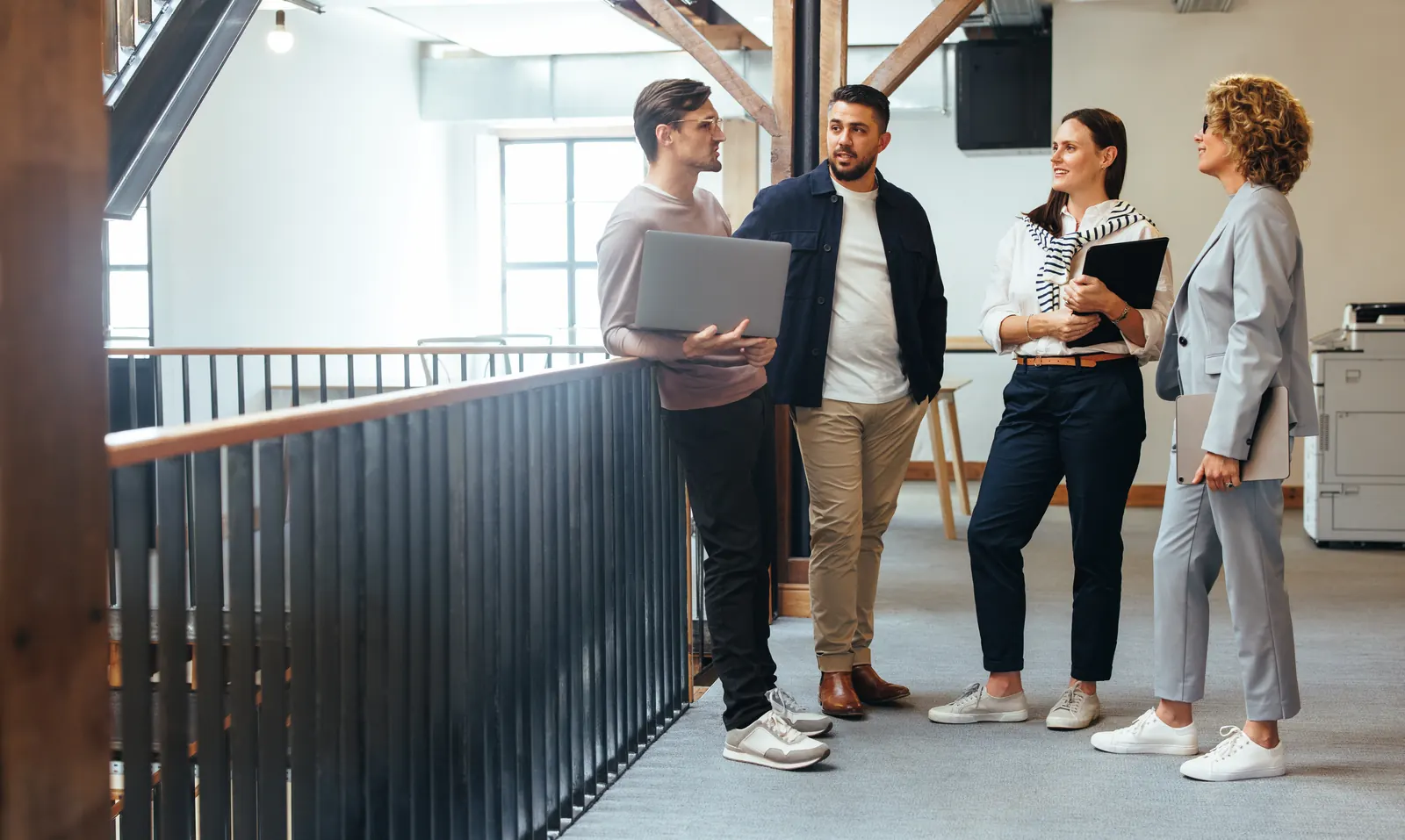 Four colleagues discussing work around an open laptop in an office corridor