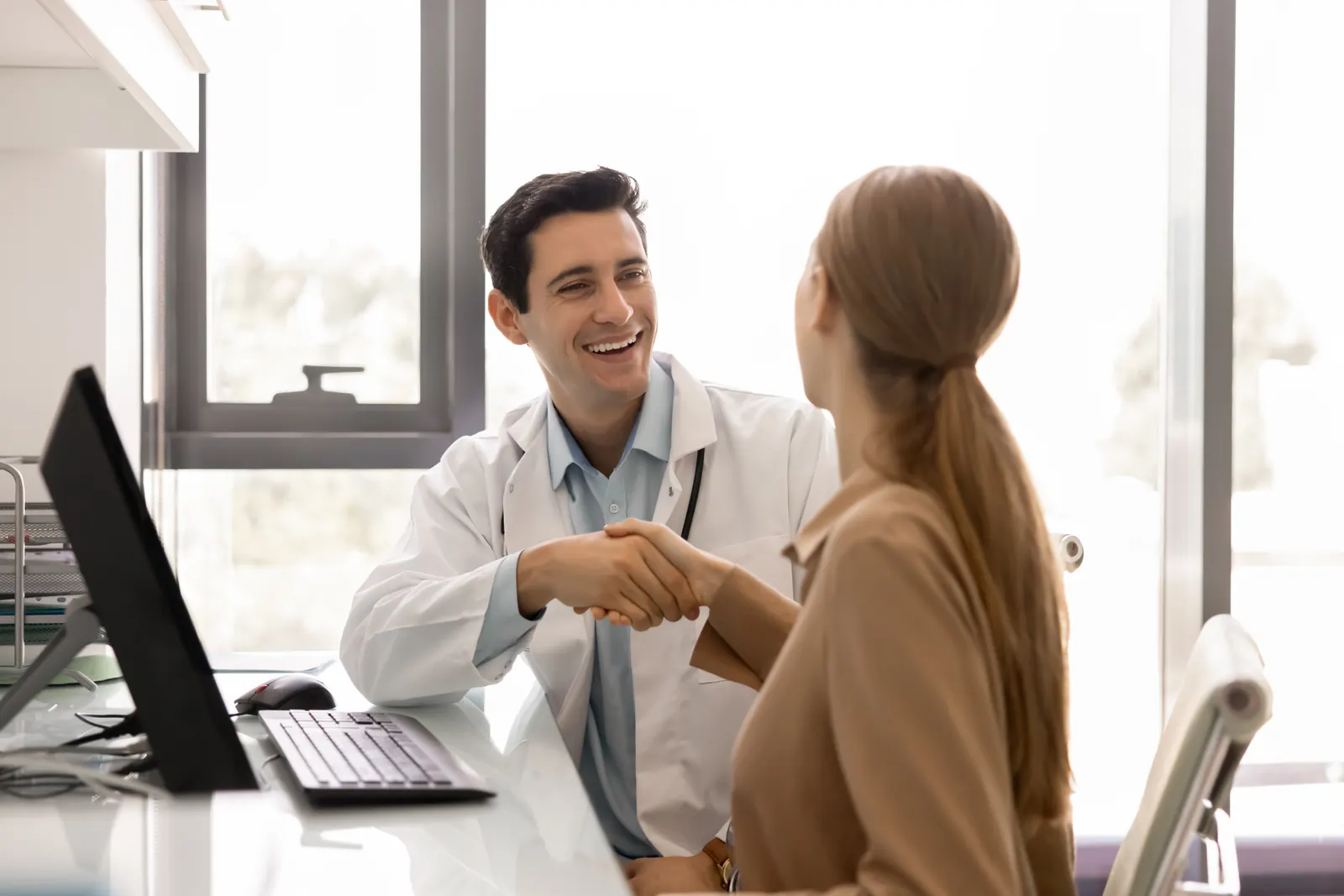 A doctor greeting a patient with a handshake across a desk