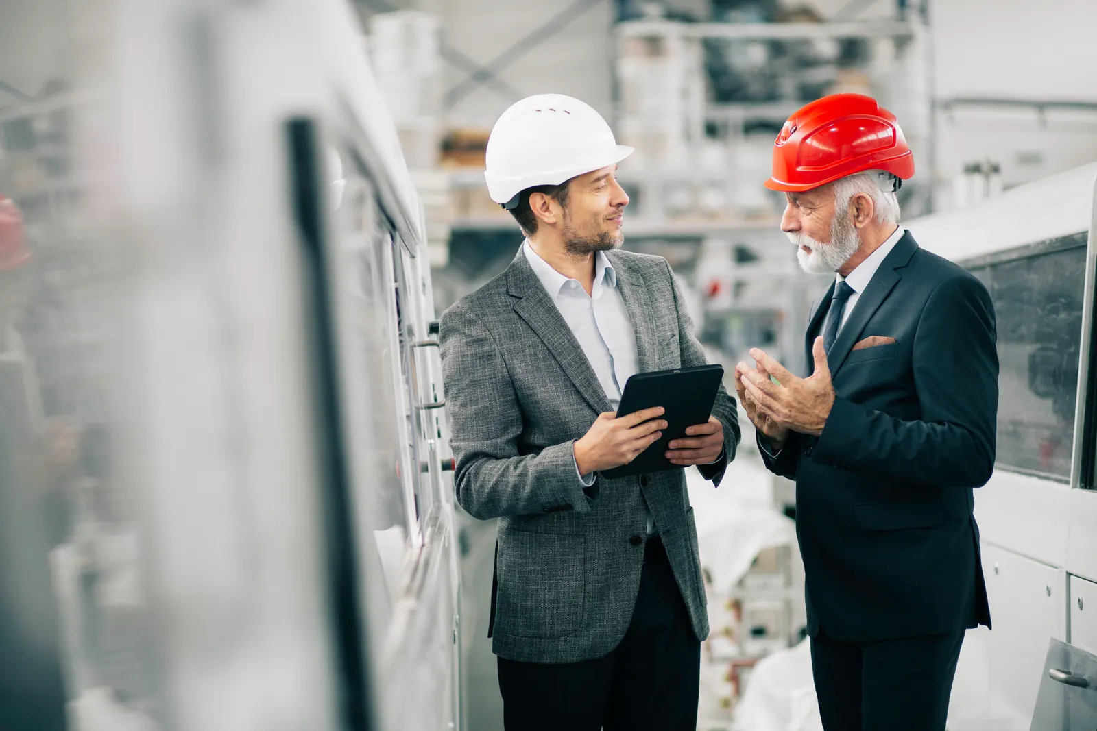 Two engineers in hard hats consulting a tablet inside an industrial facility