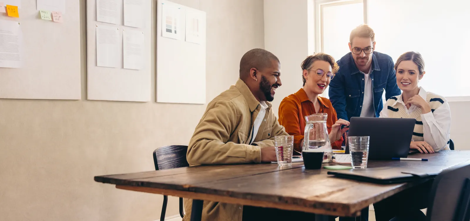 Illustrative stock photograph of four people reviewing a laptop together at a wooden meeting table