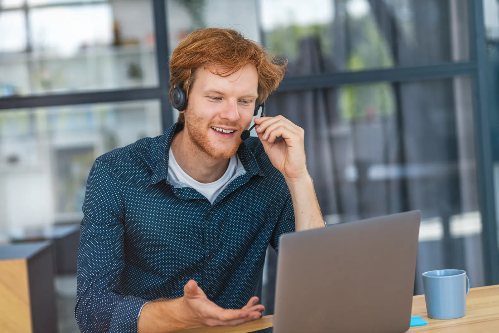 Professional wearing a headset during a laptop conversation in a blue-toned office