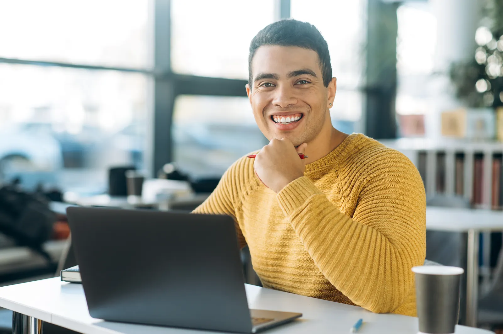 A business owner in a mustard jumper working at a laptop in a bright office