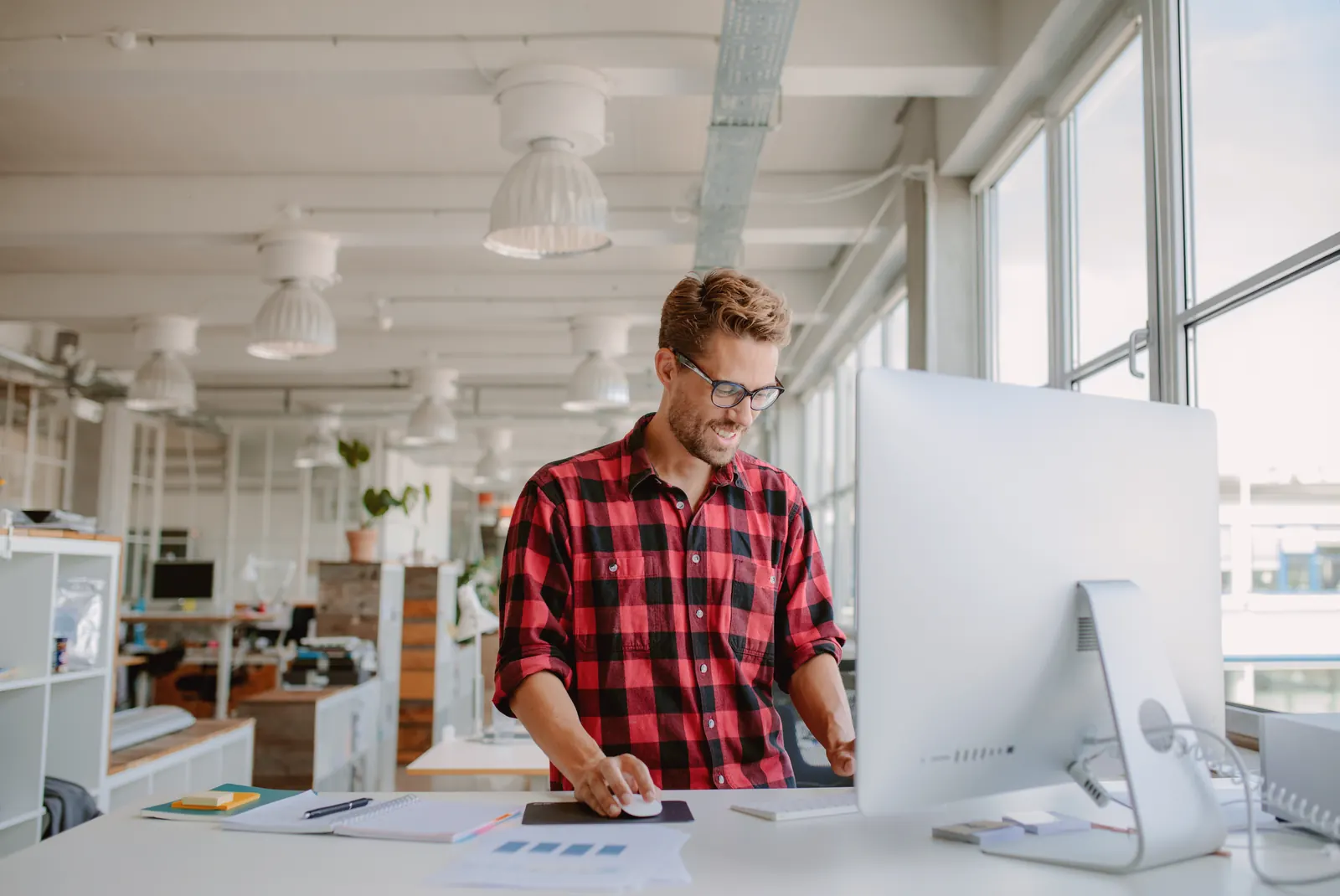 A specialist in a checked shirt working at a desktop in an open office