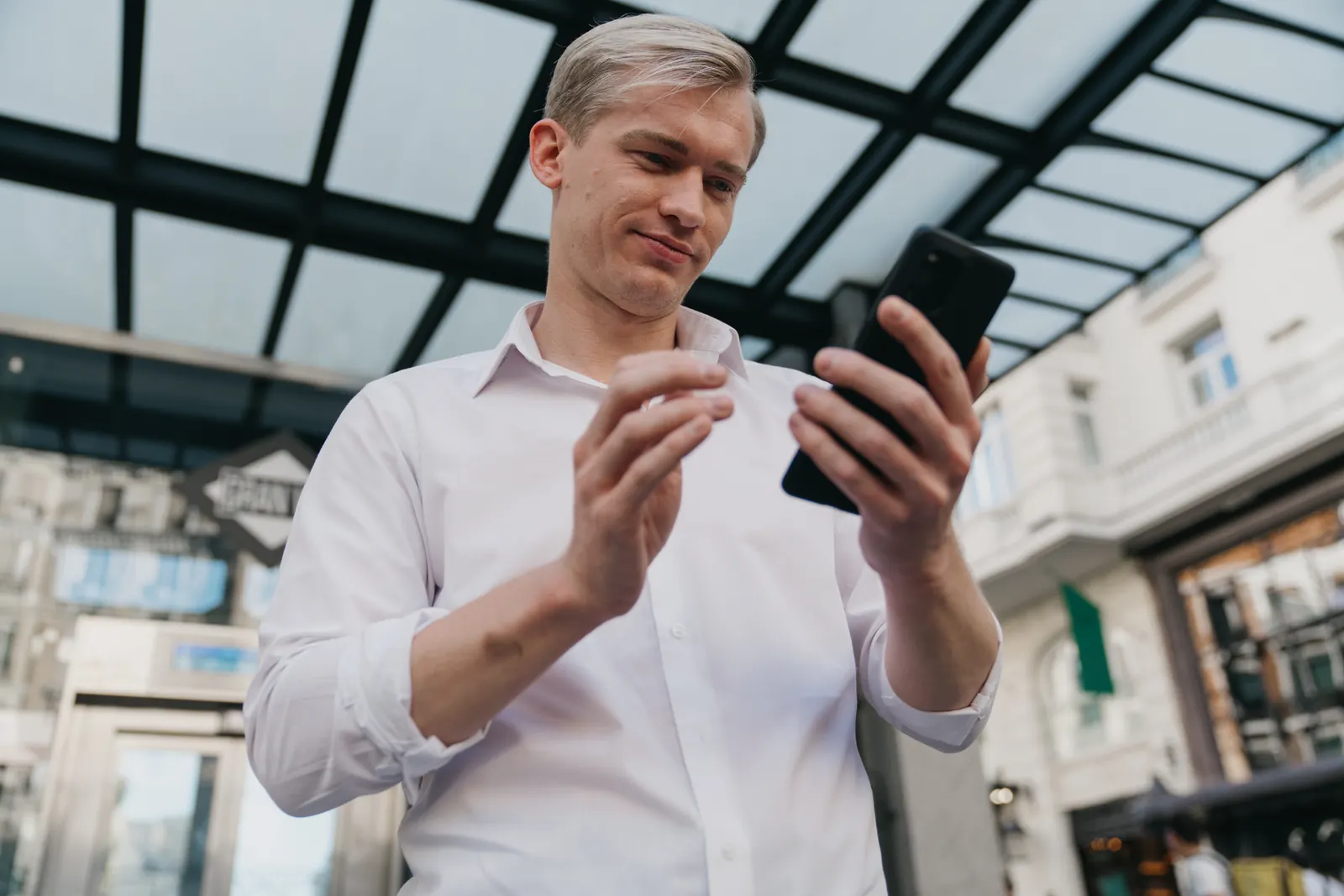 A professional checking a smartphone beneath an outdoor glass canopy