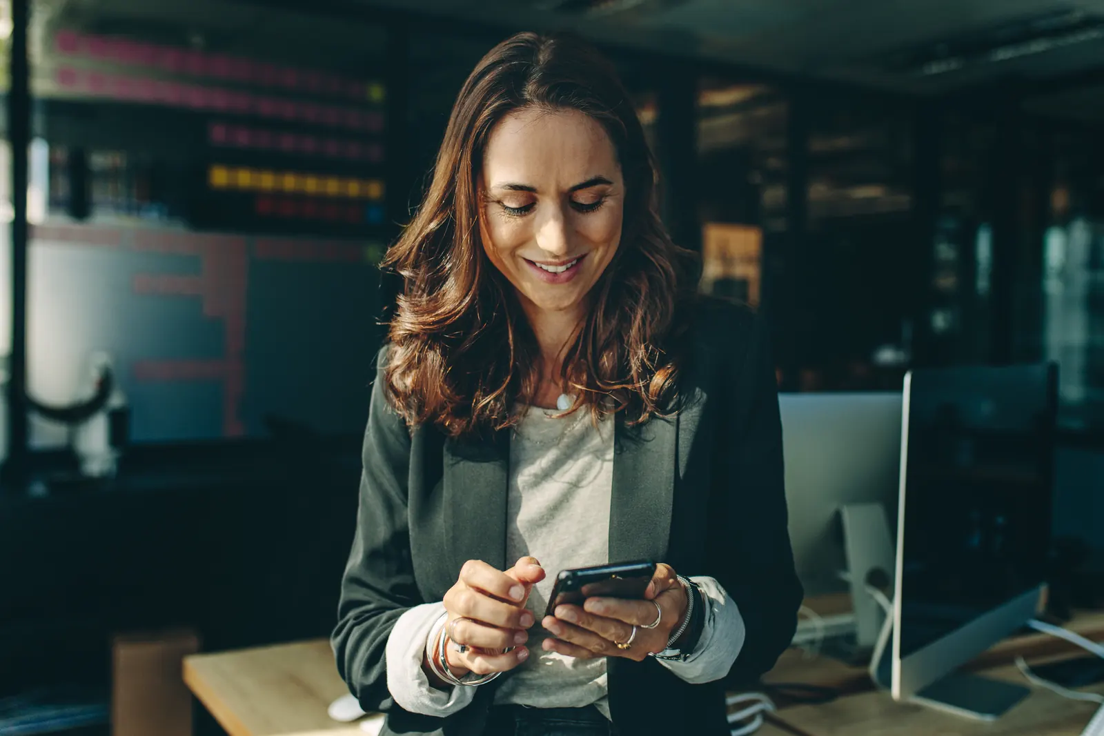 Professional checking a smartphone in a warmly lit, blue-toned workspace