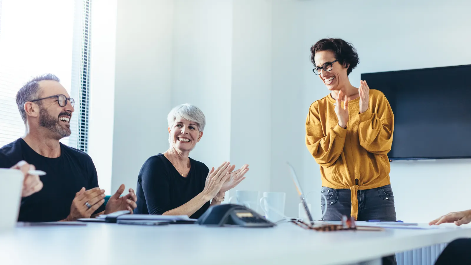 A workshop facilitator in a mustard blouse discussing a plan with seated colleagues