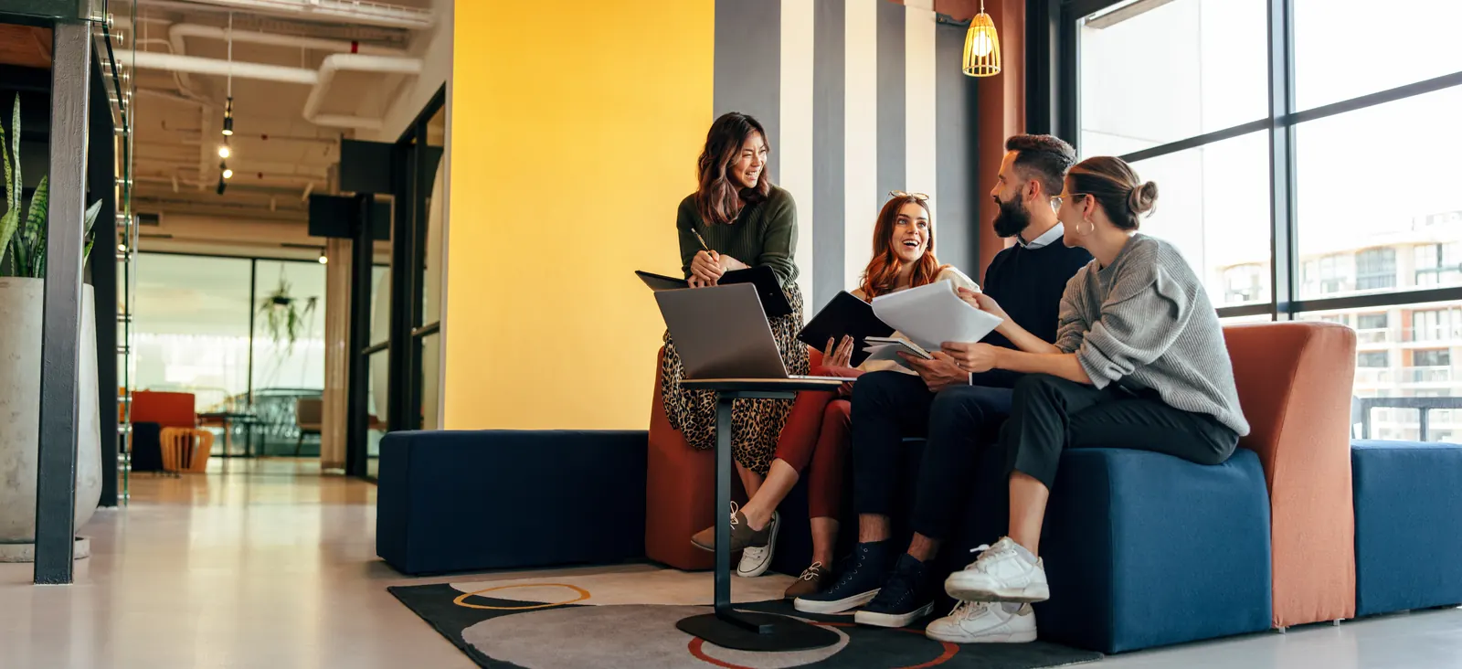Colleagues discussing a project in a bright office seating area with orange upholstery
