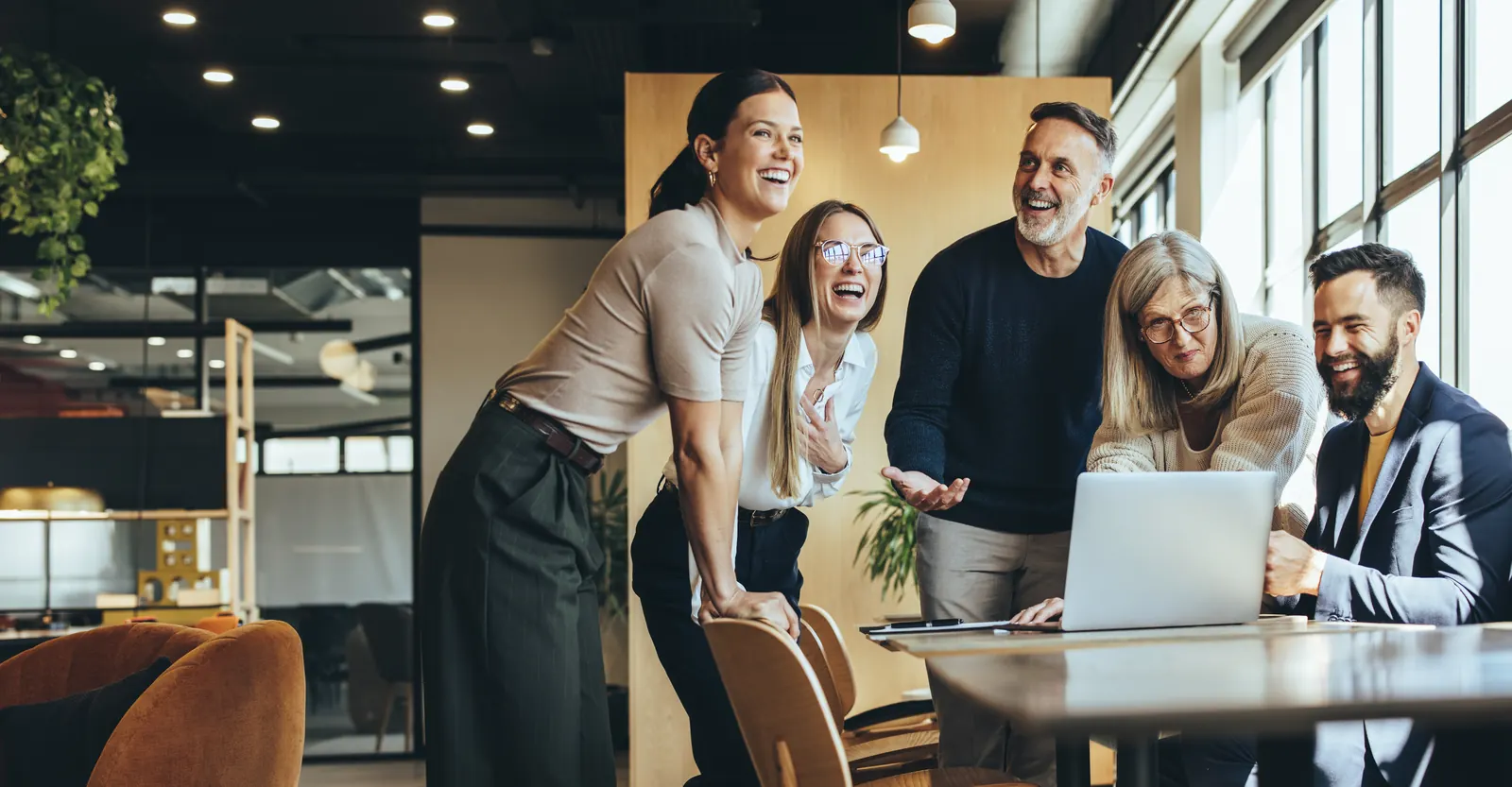Five colleagues gathered around a laptop in a bright shared workspace.