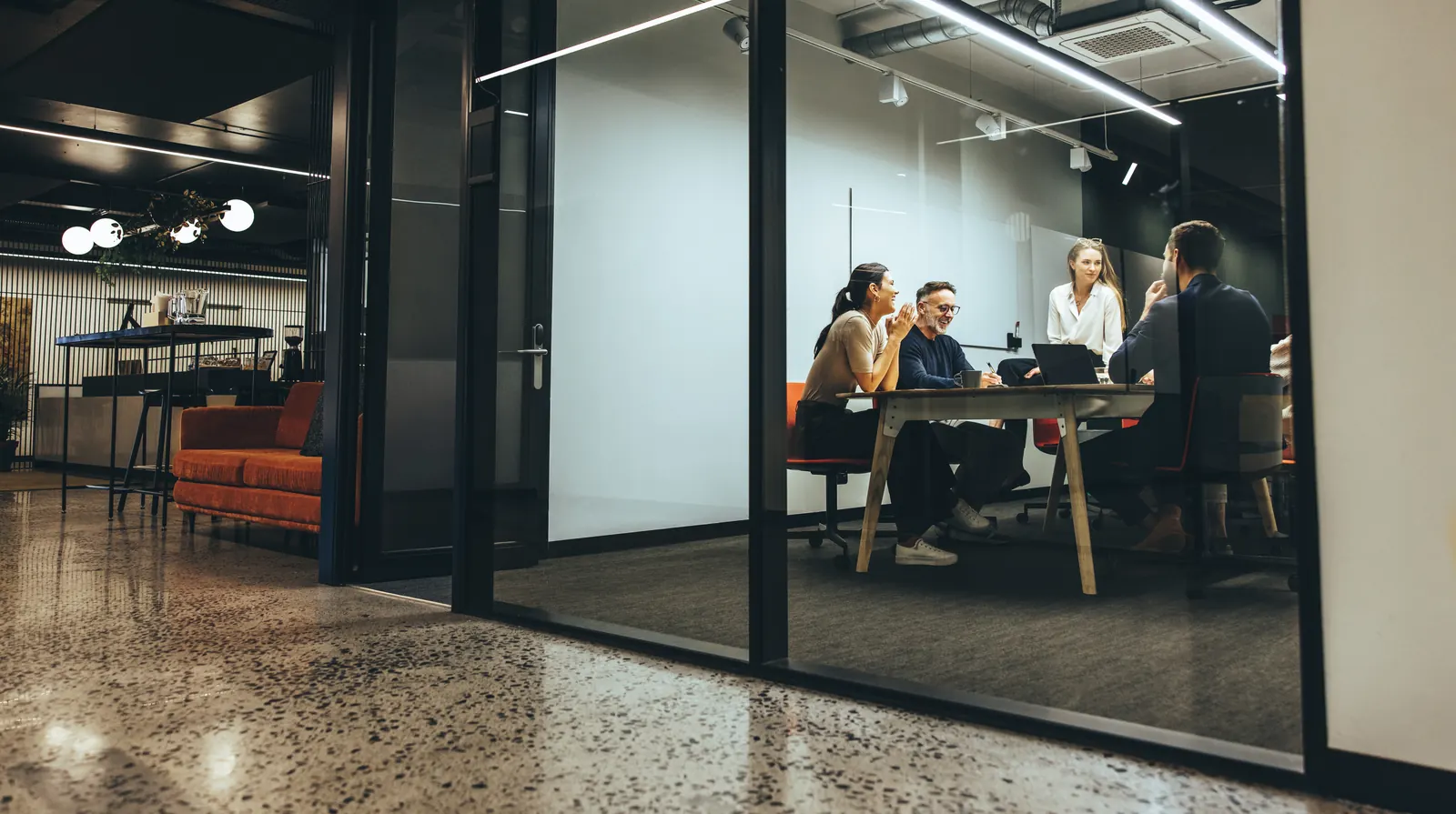 A project team meeting in a glass-walled office beside an open workspace
