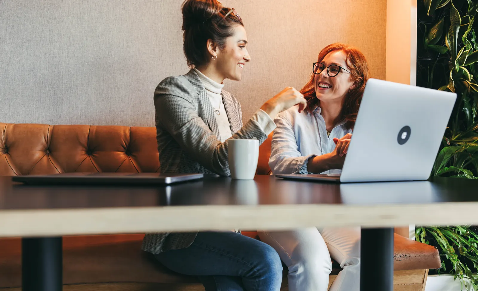 Two colleagues discussing an improvement beside a laptop in a warm orange workspace