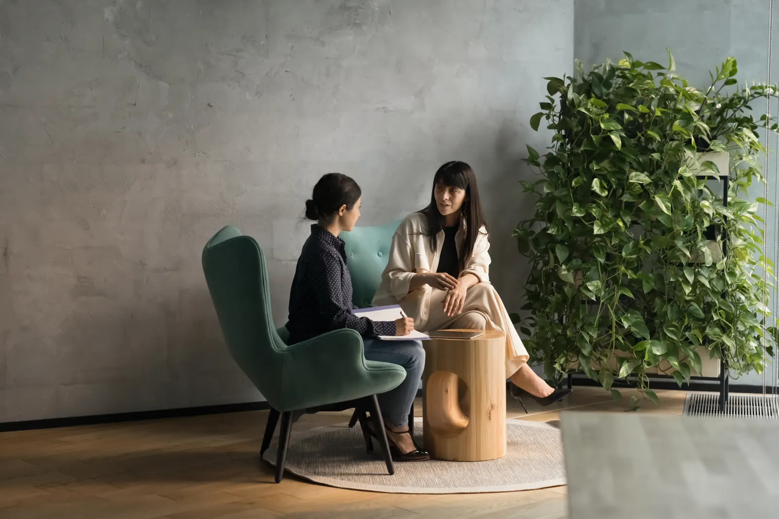 Two colleagues discussing ideas and taking notes in a quiet office seating area.