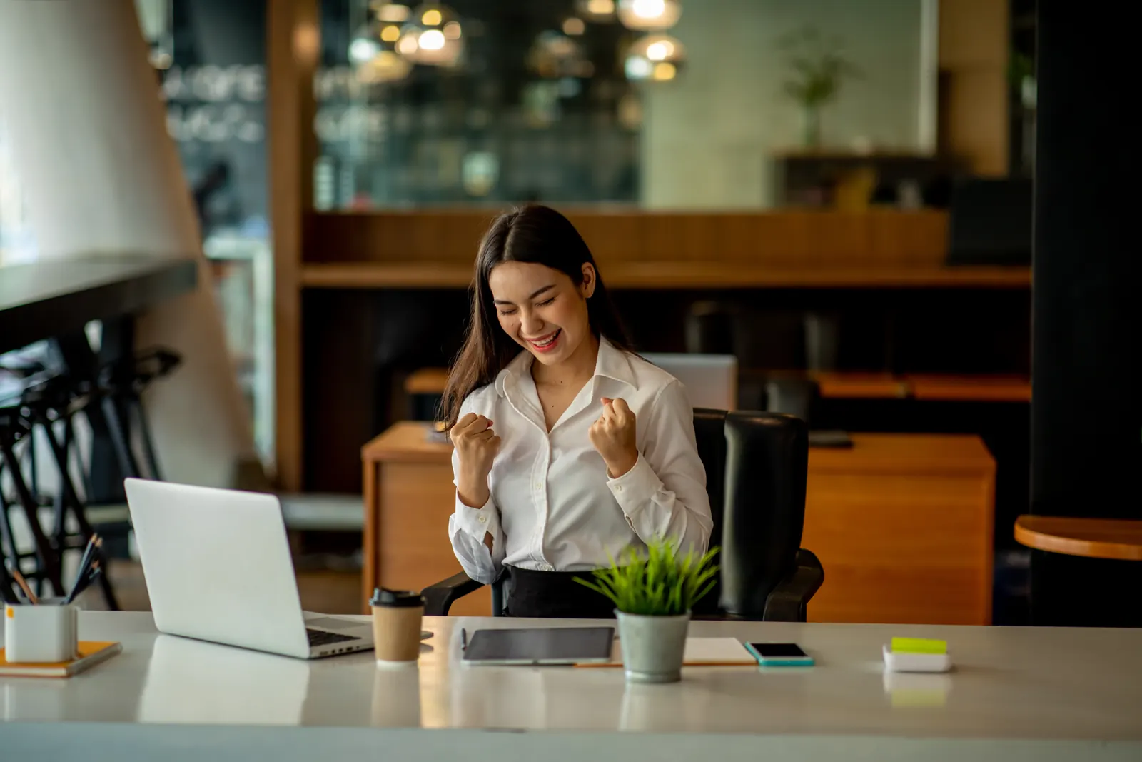 A woman raising her fists in celebration beside an open laptop