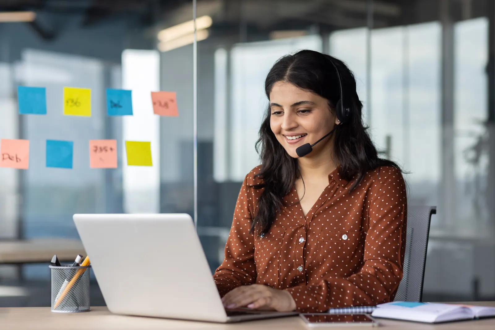 Headset-wearing professional working at a laptop with reference notes beside her