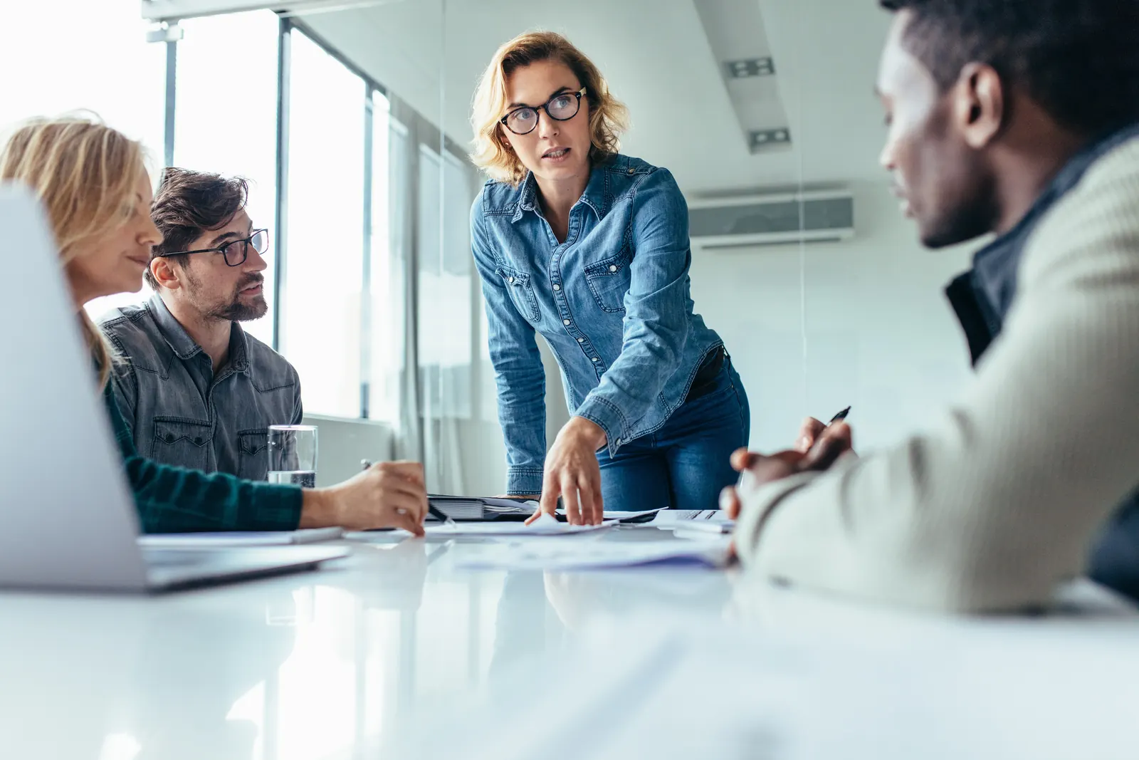 A facilitator and colleagues discussing a delivery plan across a meeting table