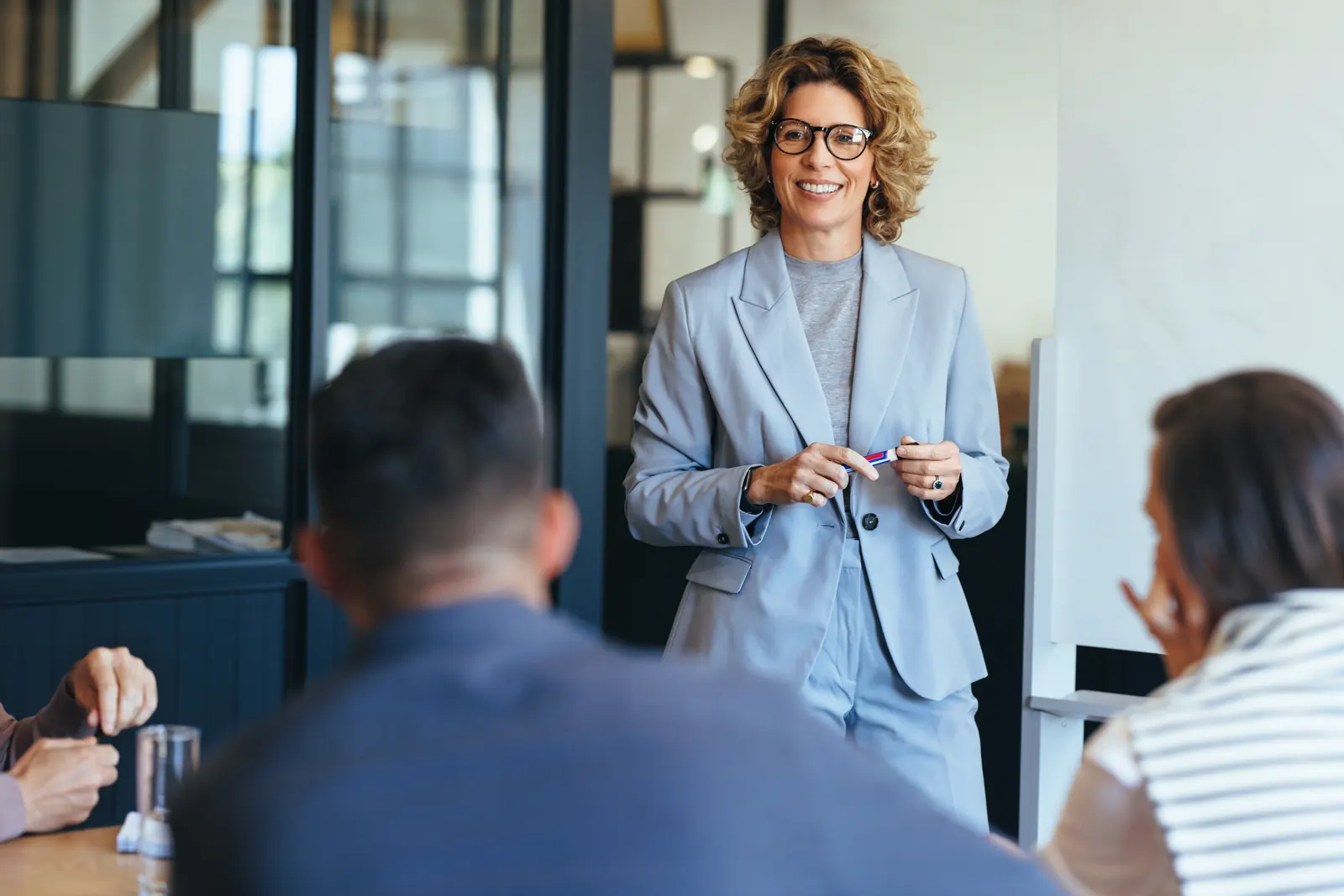 A colleague in a blue blazer leading an open discussion with her team around a meeting table