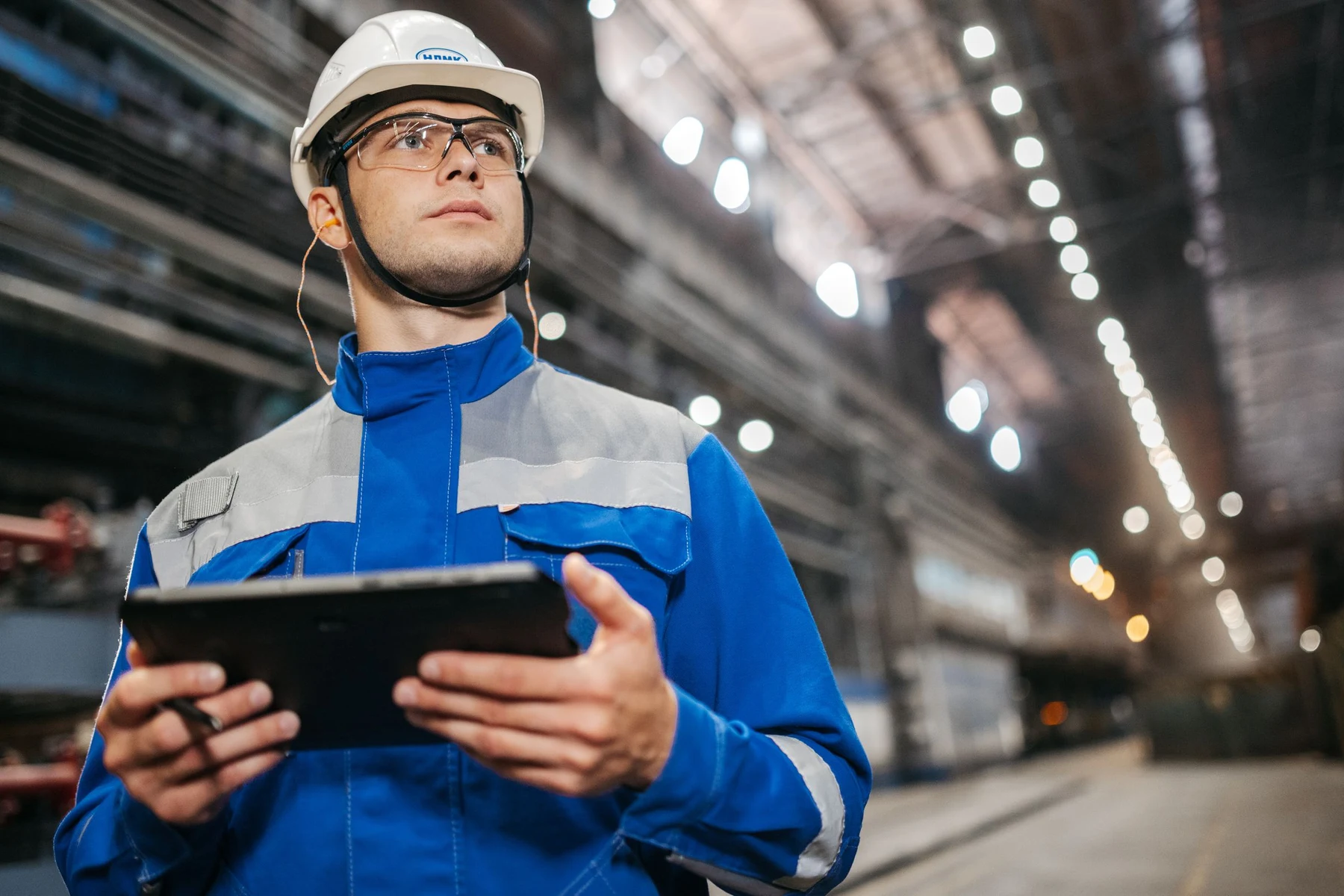A factory worker in blue safety clothing checking information on a tablet