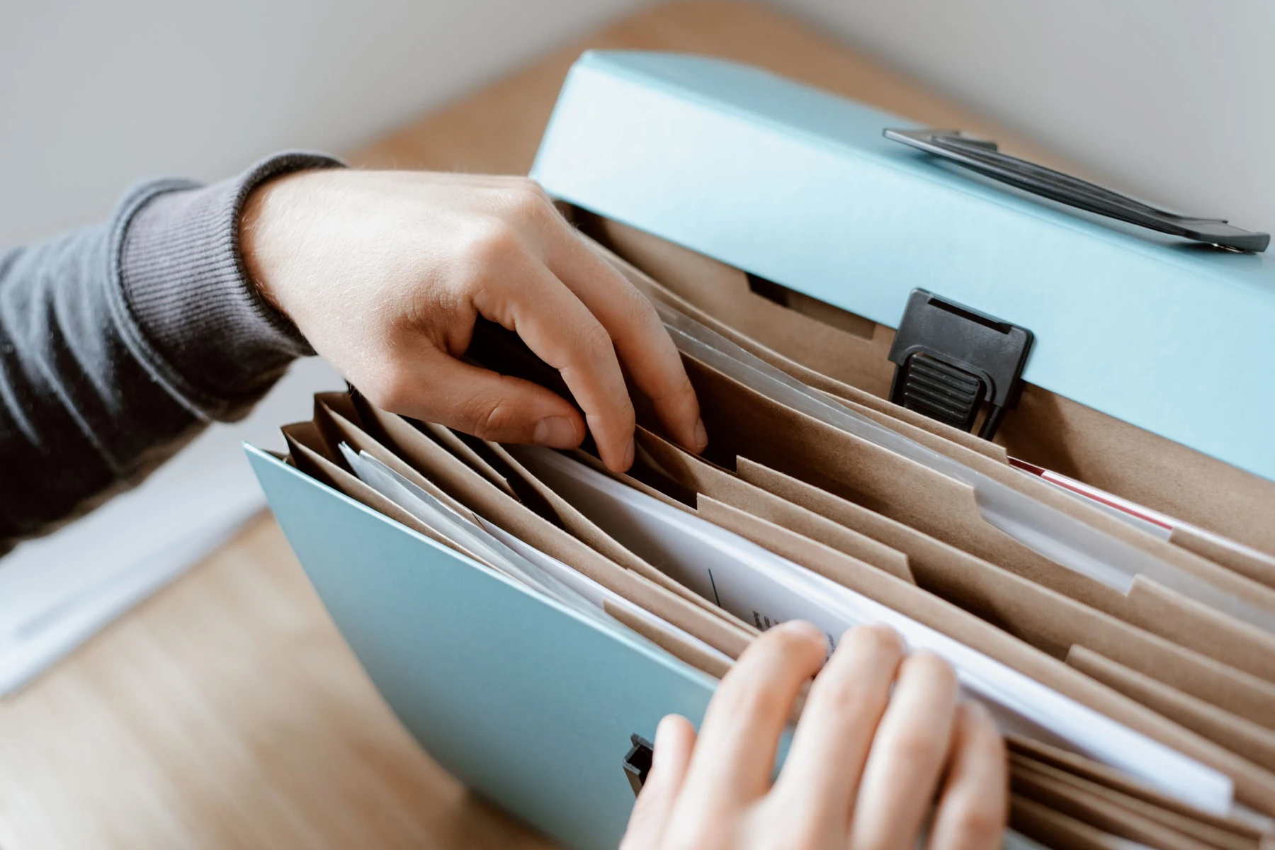 Hands selecting a document from an organised blue file folder on a wooden table