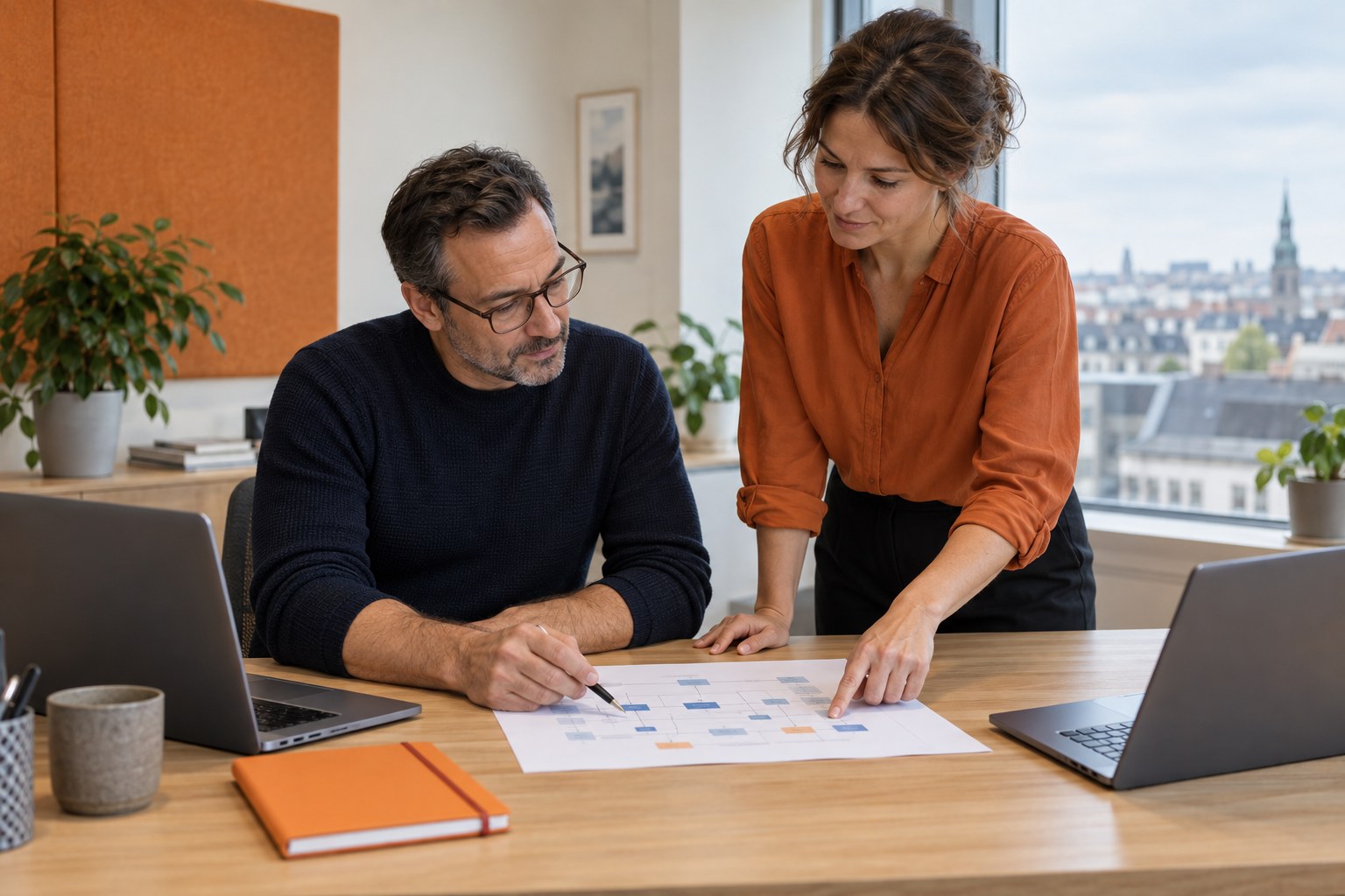 Two data architects reviewing a printed system diagram at an oak desk
