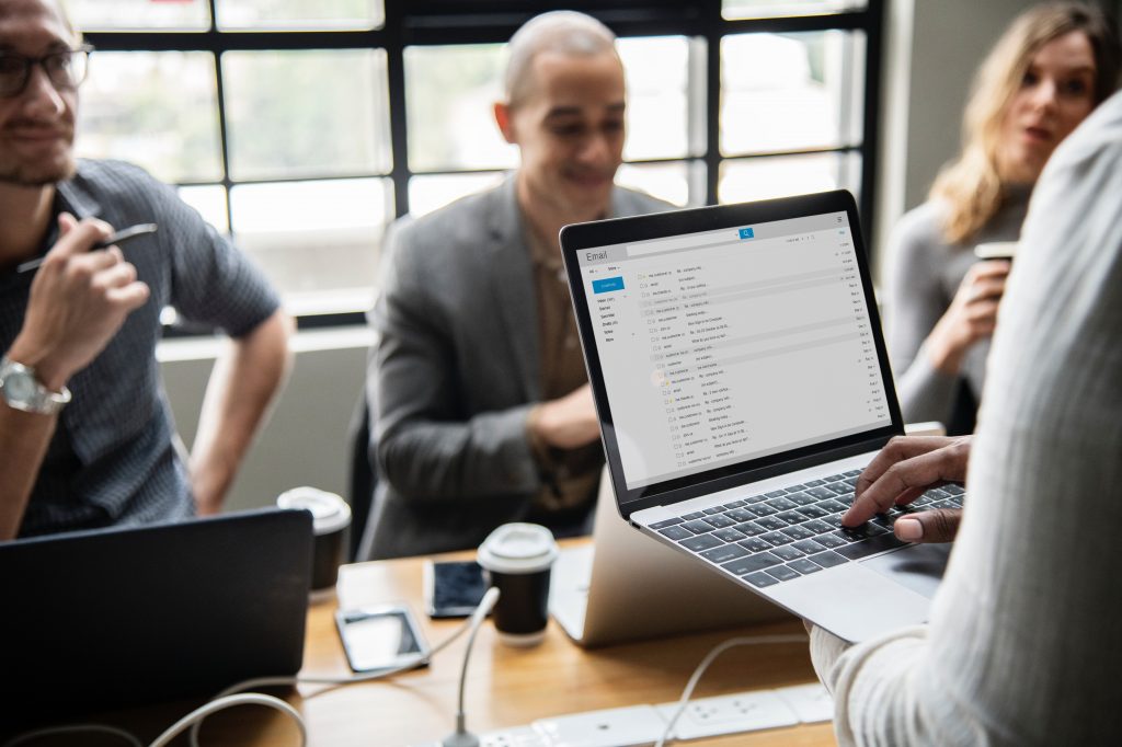 A group of people in a business meeting drinking coffee while presenter is checking email on a laptop